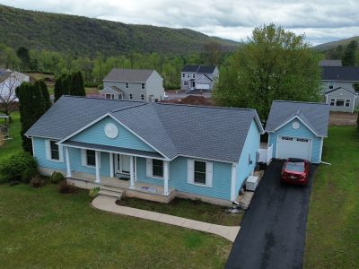 Beautiful blue house with new roof and driveway, showcasing RWB Roofing & Construction services.